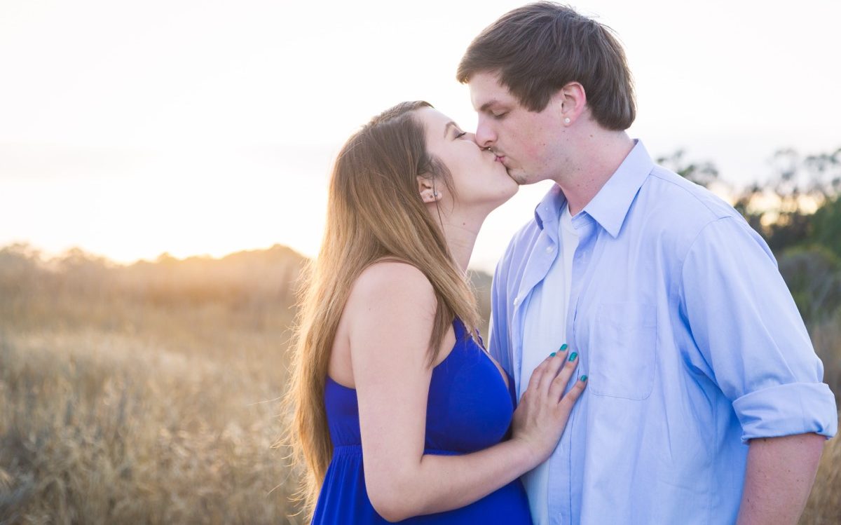 Expecting couple kissing in a golden meadow at sunset