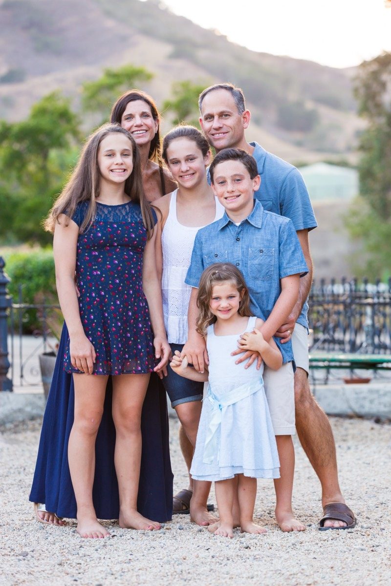 Family of six standing together on a sunlit outdoor staircase