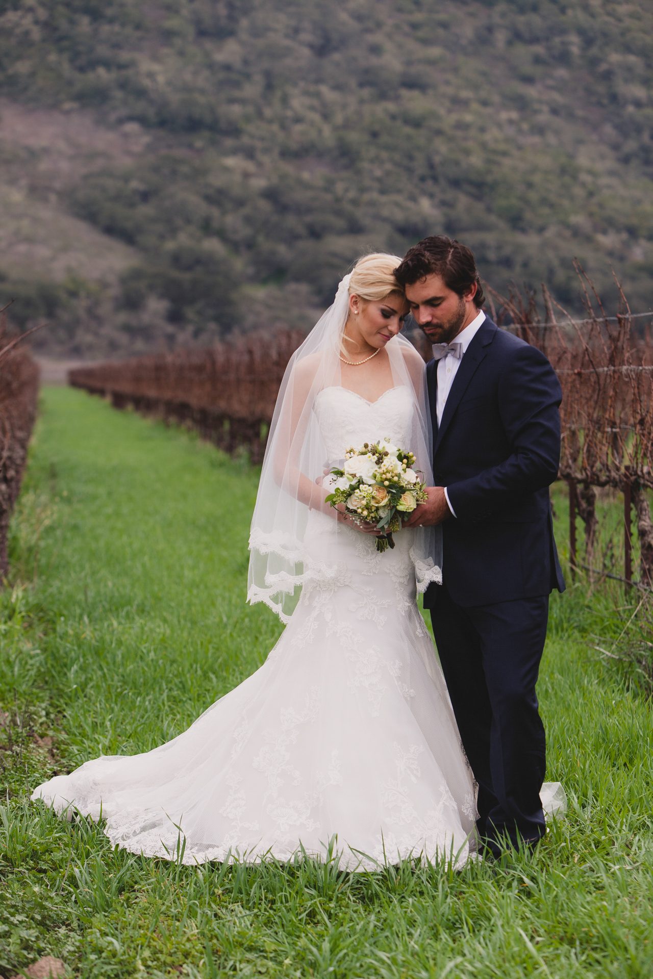 Bride and groom standing together in a green vineyard row under soft overcast light