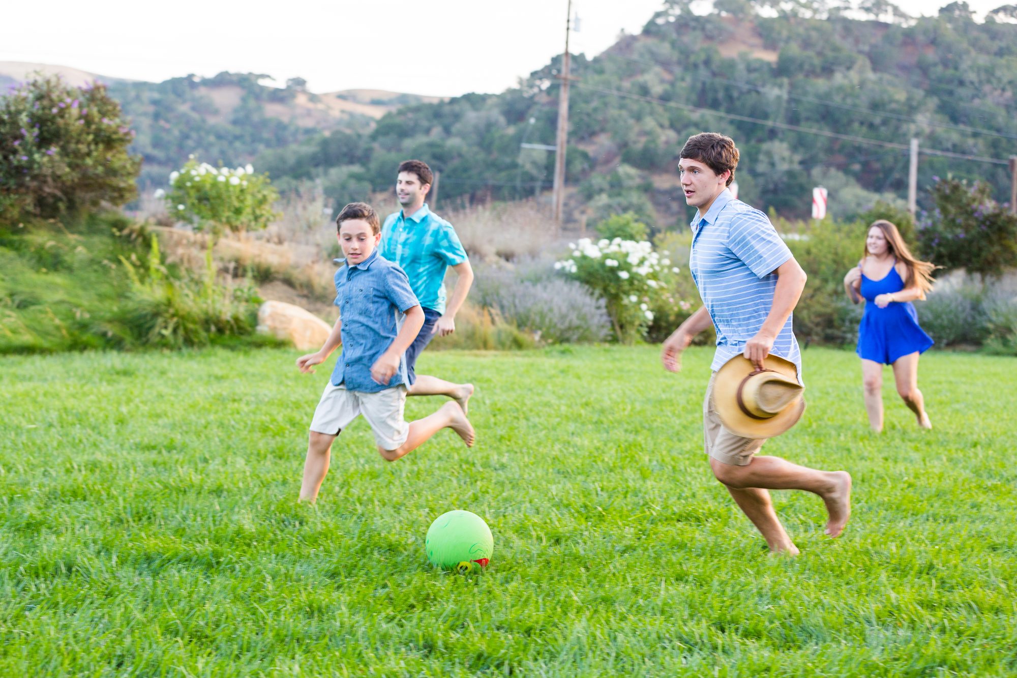 Barefoot boys and young adults chasing a green ball across a lawn at golden hour