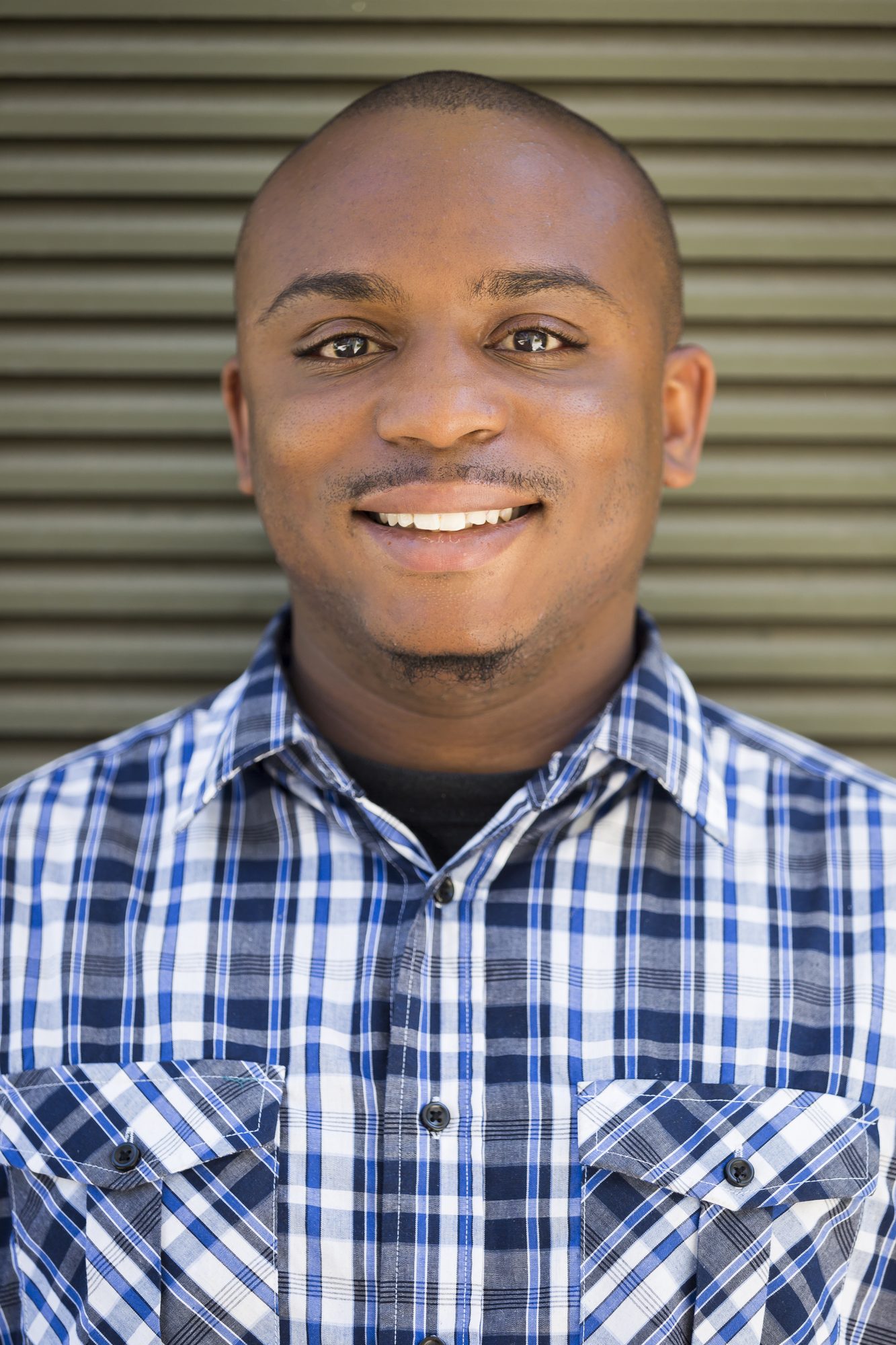 Smiling man in a blue plaid shirt in front of a metal roll-up door