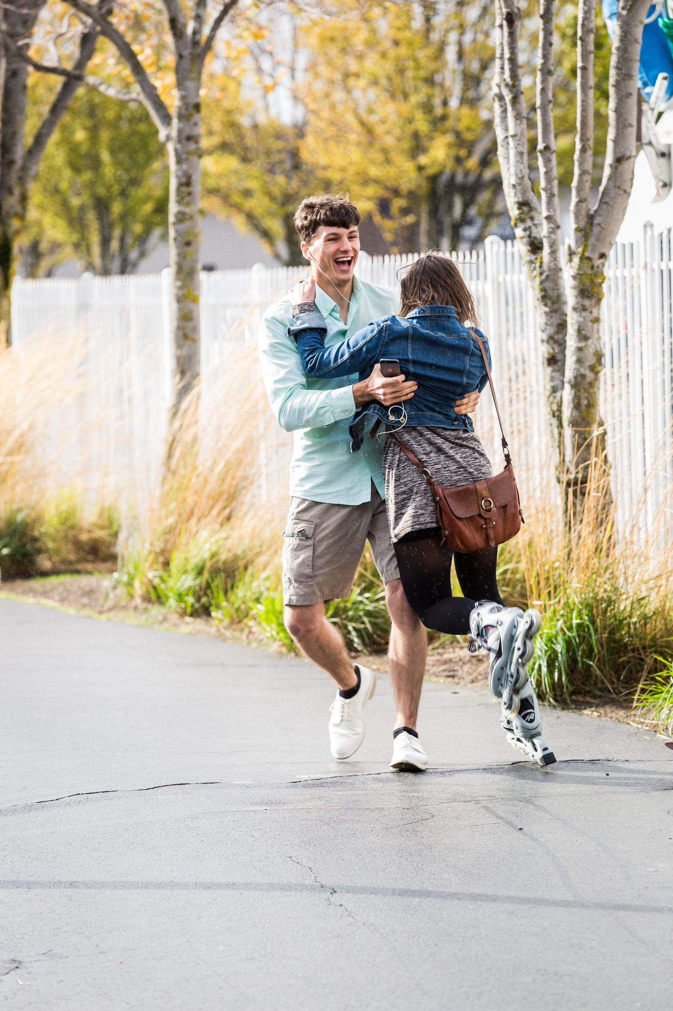 Laughing couple on roller skates, him carrying her down a tree-lined path
