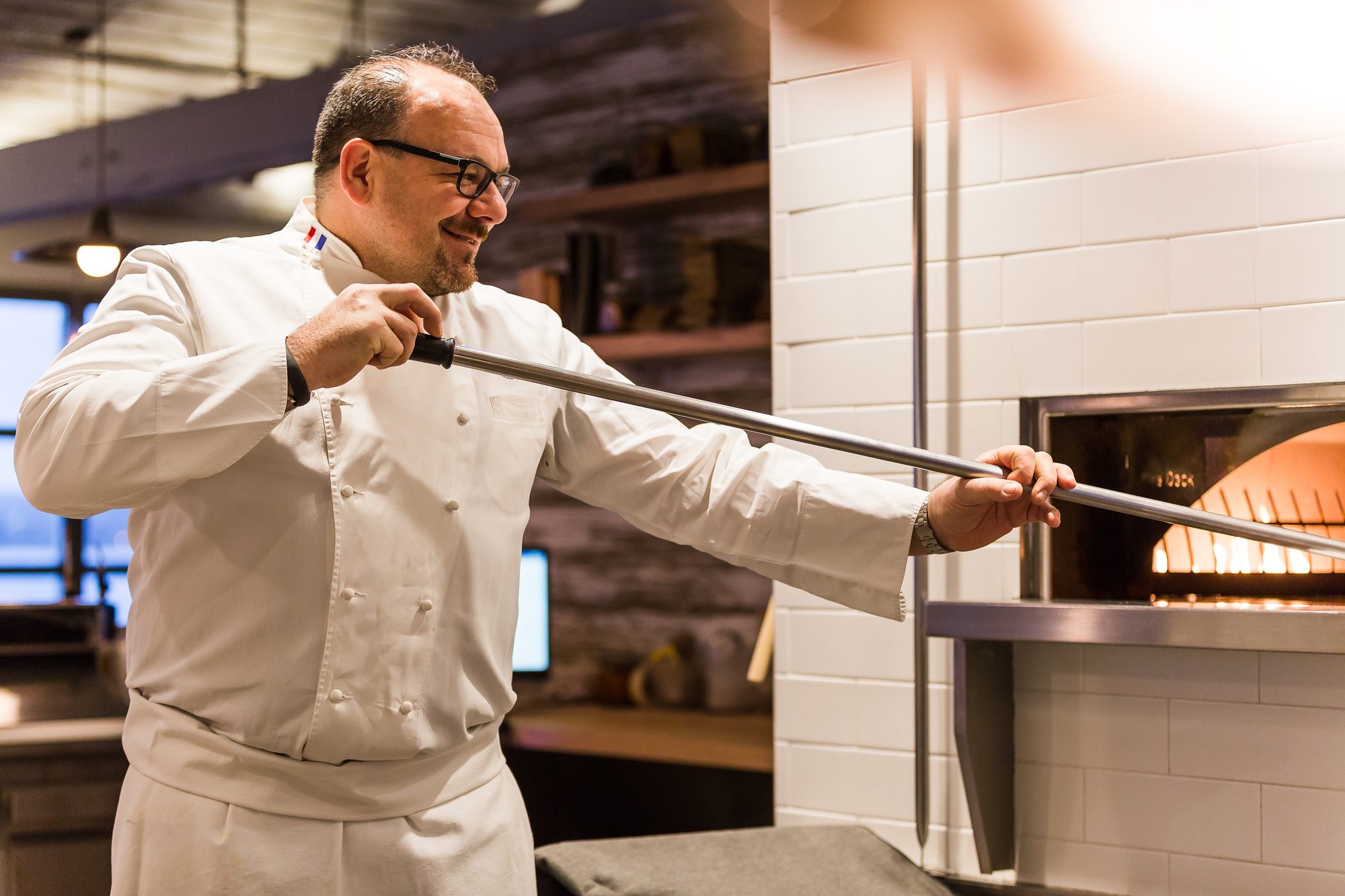 Chef in whites sliding a pizza into a wood-fired oven