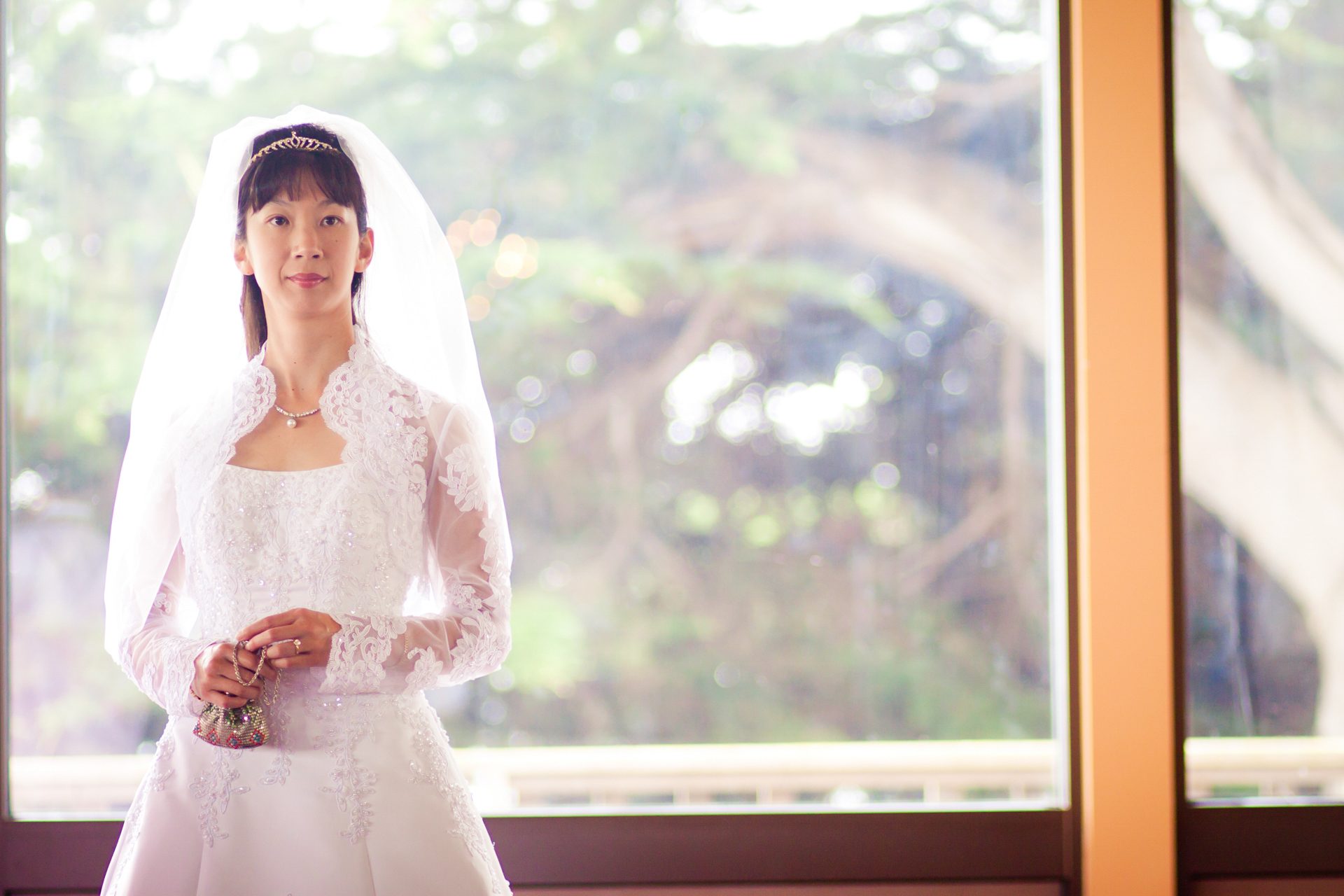 Bride in her veil standing by a bright window, holding her bouquet