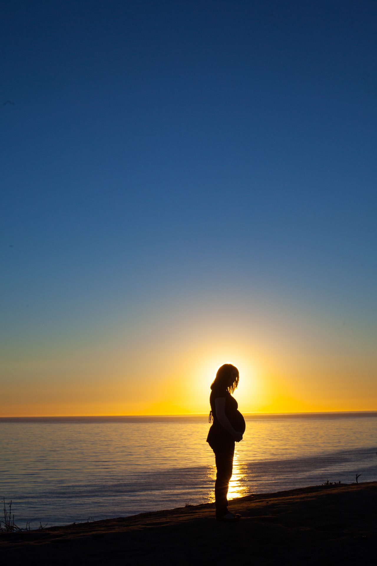 Expecting mother silhouetted against the setting sun at the beach