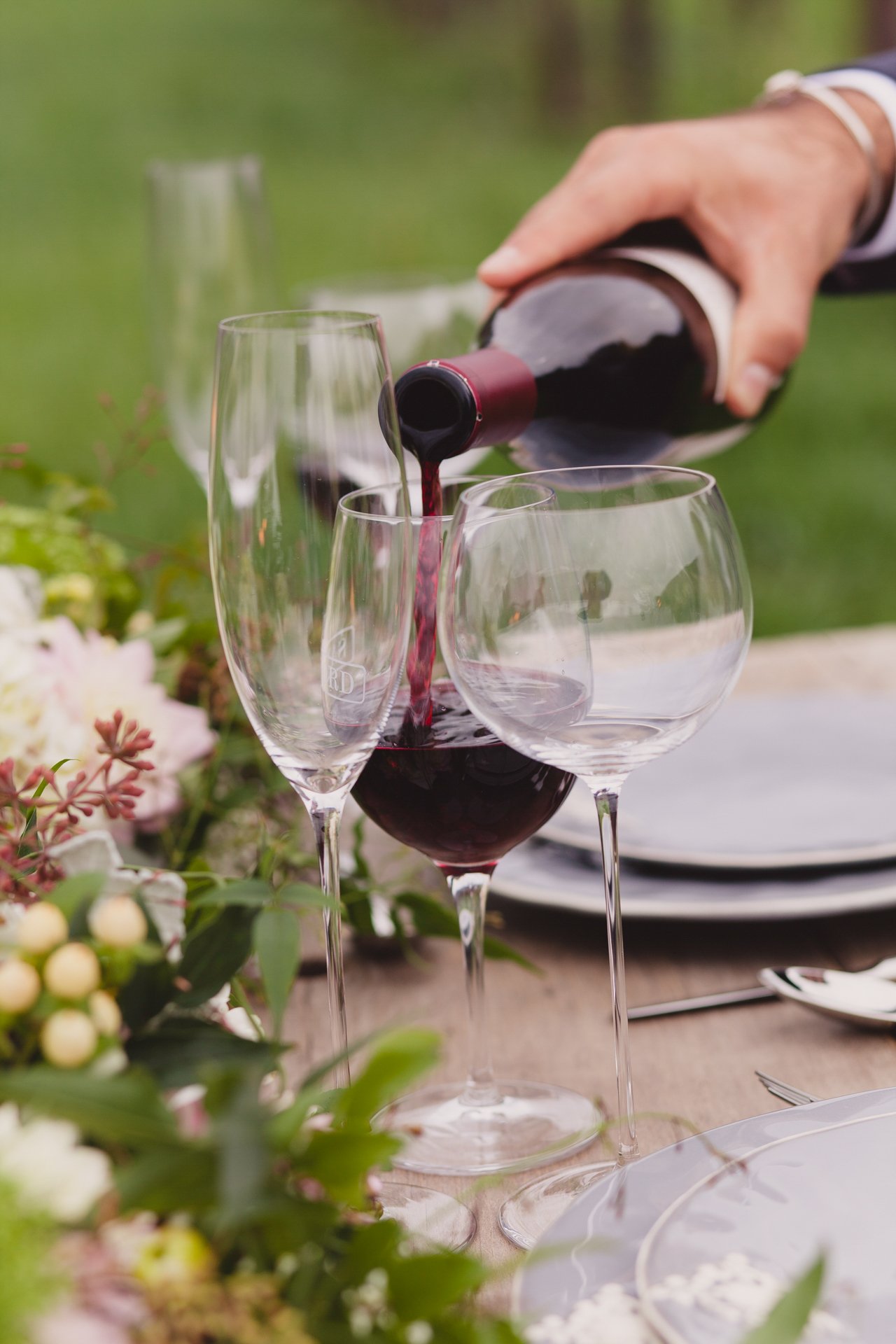 Red wine being poured into a glass at an outdoor table set with flowers and crystal stemware