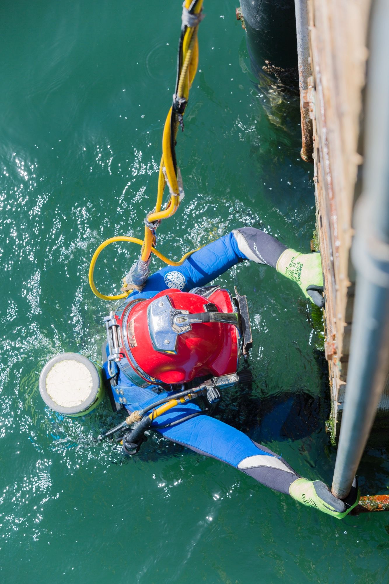 Overhead view of a diver in a red helmet descending a ladder into green ocean water