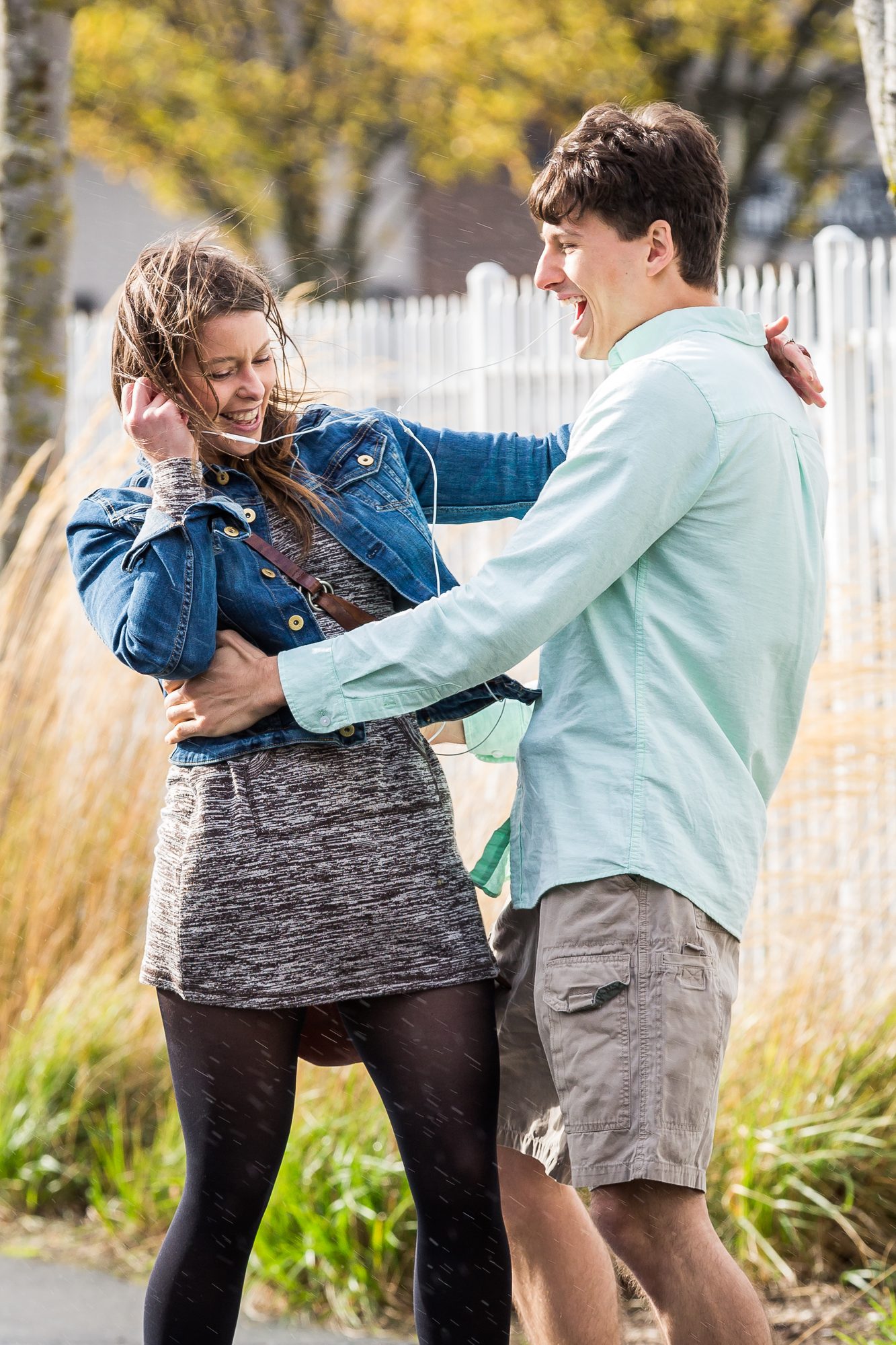 Couple laughing together outdoors, she in a denim jacket, beside tall autumn grasses