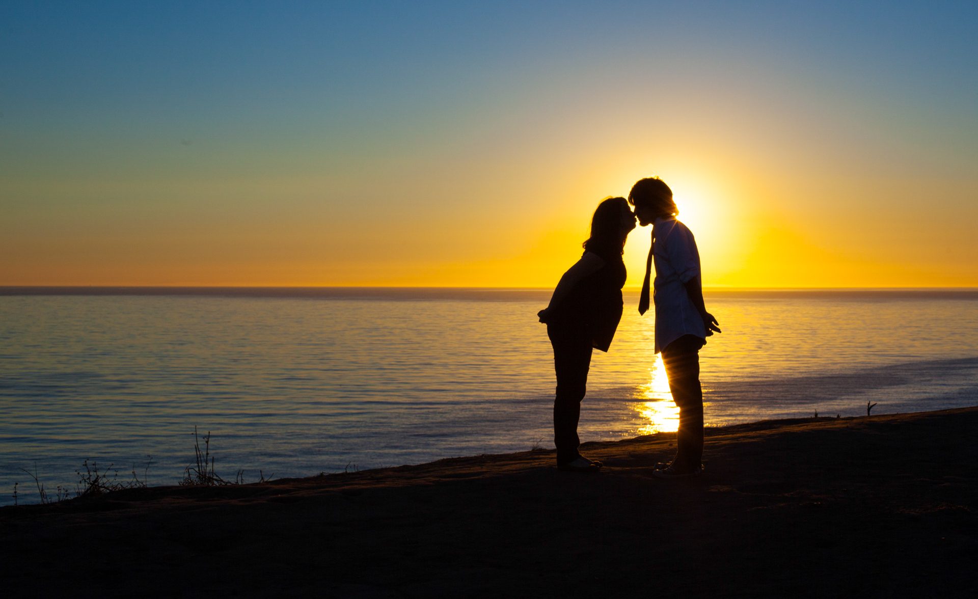 Couple silhouetted in a kiss against the setting sun over the Pacific