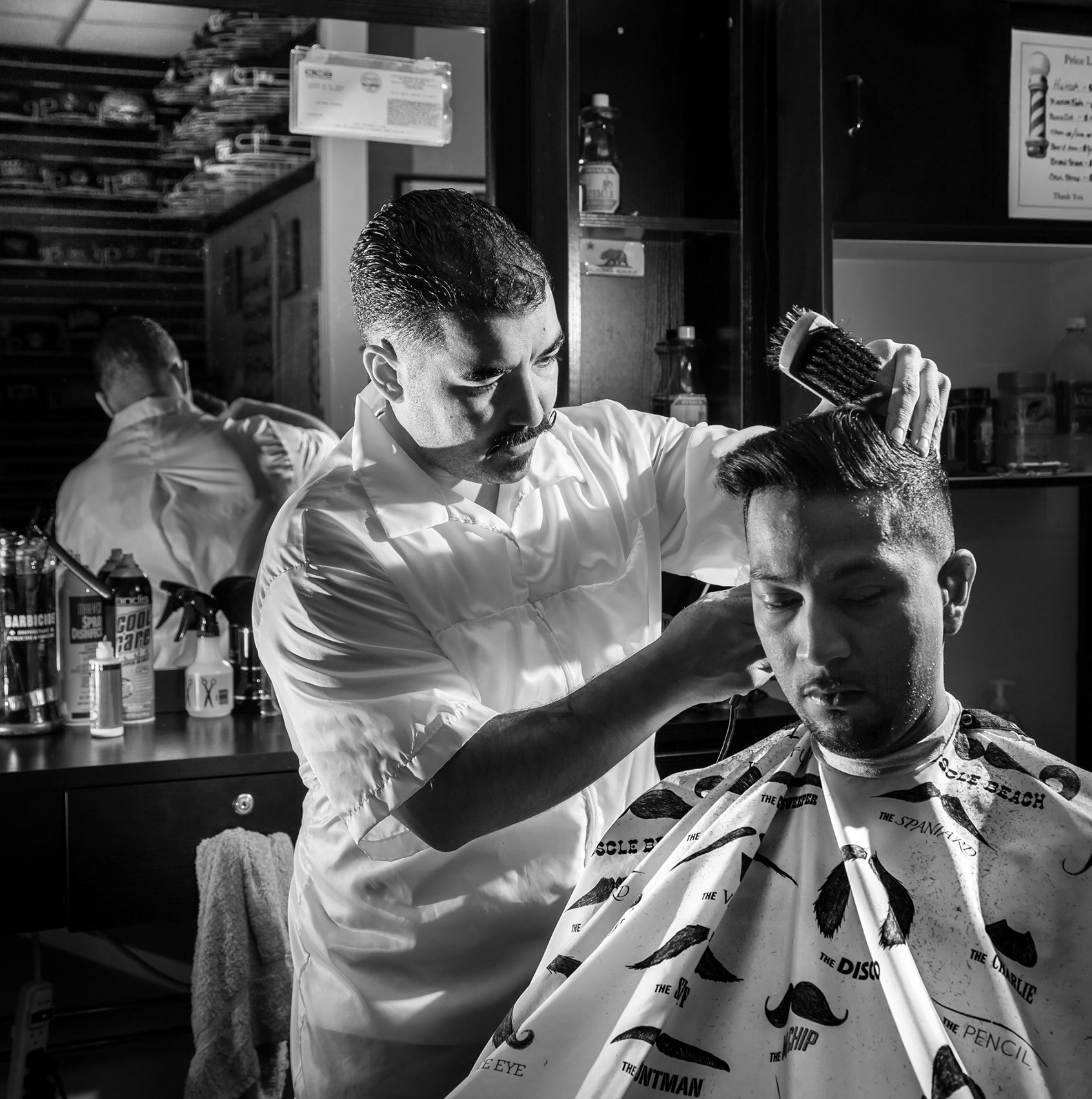 Black and white image of a barber trimming a customer's hair in a classic barber shop
