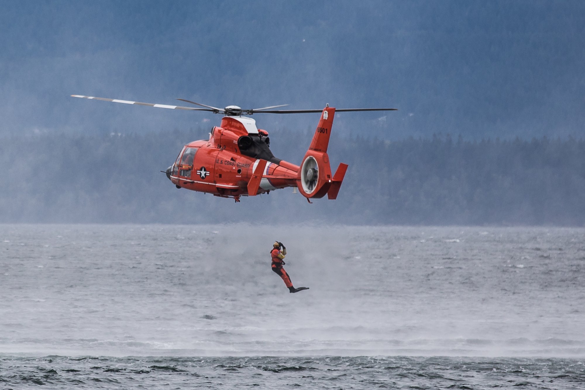 Rescue helicopter hovering over the bay as a rescue swimmer is lowered toward the water during a waterfront festival demo