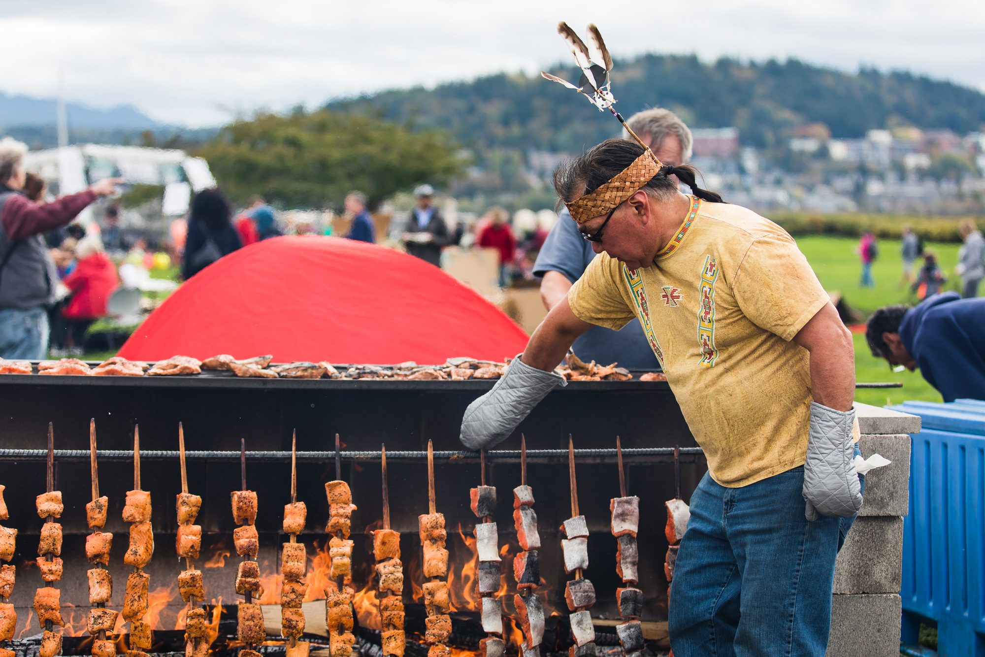 Cook in a bandana grilling rows of skewered salmon over an open fire pit at an outdoor food festival