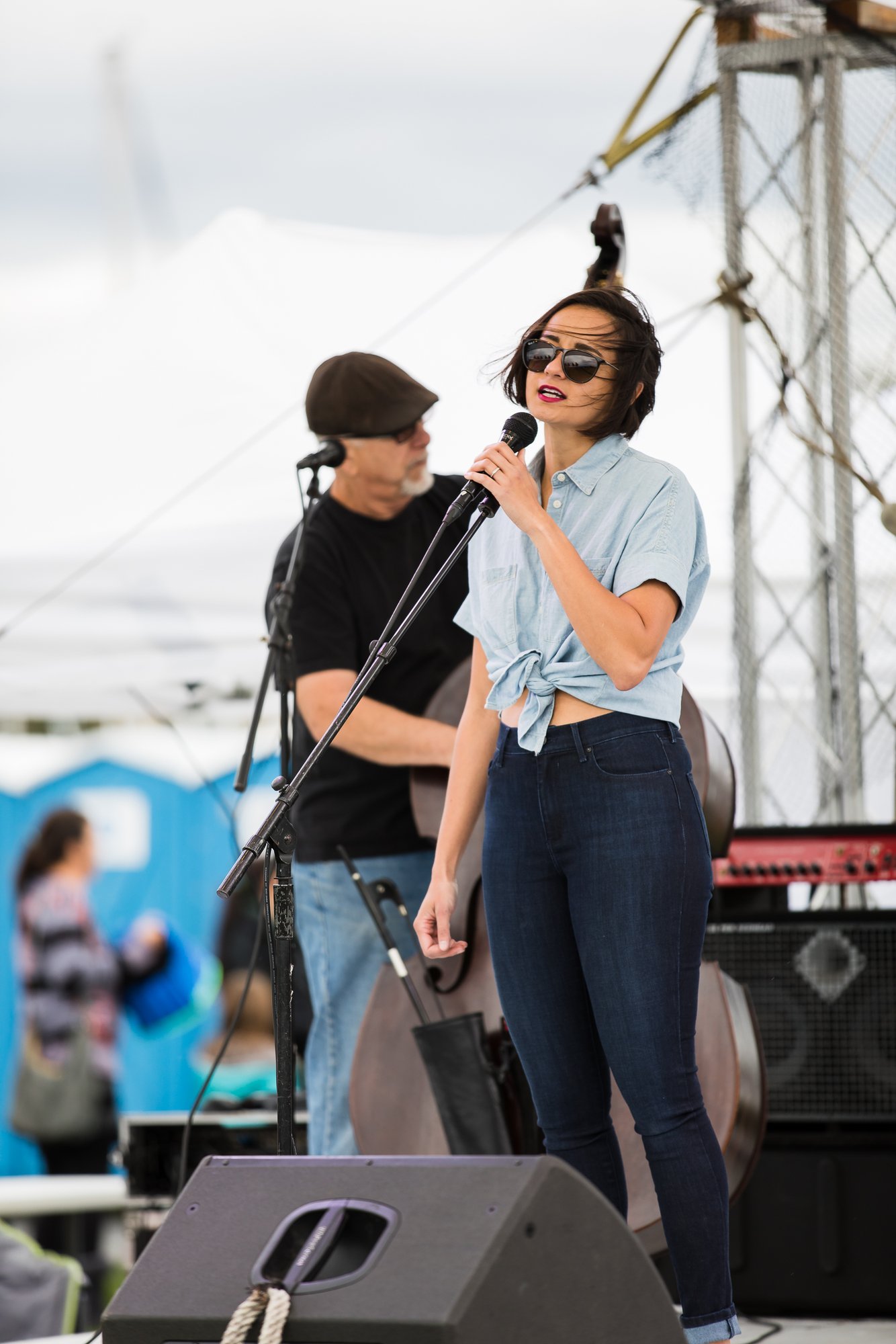 Singer performing at the microphone with an upright bassist behind her on an outdoor festival stage