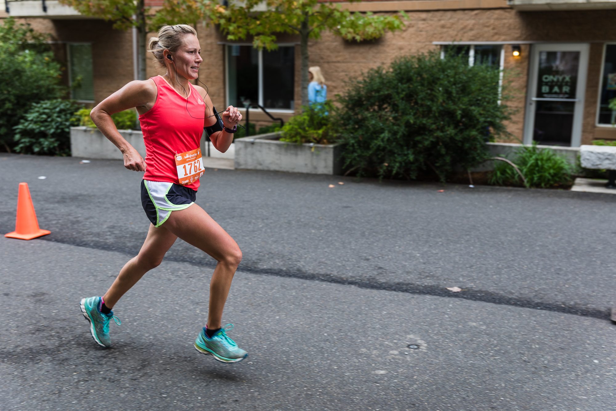 Runner in a pink top striding past orange cones on a city street during a marathon