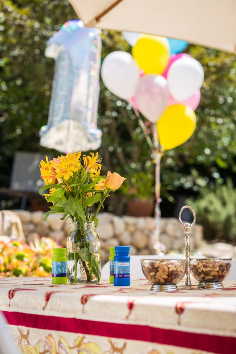 Party table with yellow flowers beneath pastel balloons and a patio umbrella