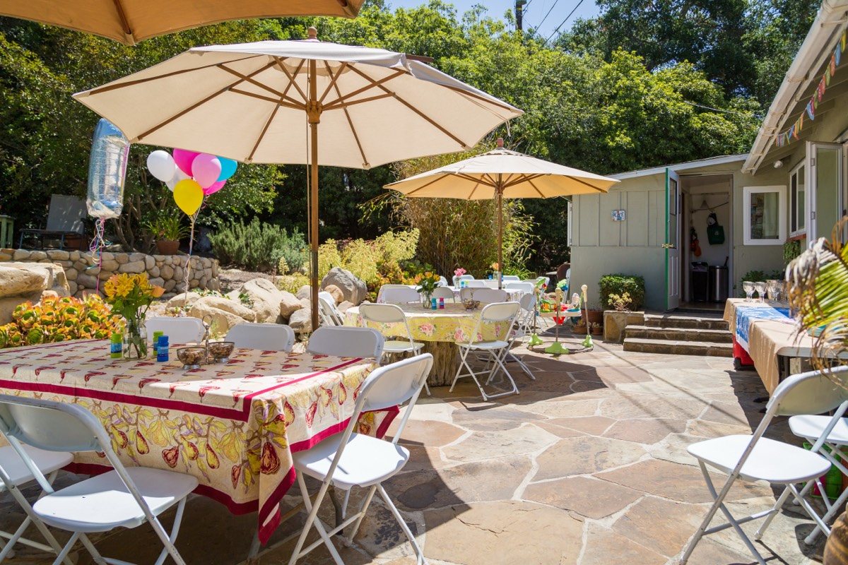 Backyard patio set for a party with umbrellas, patterned tablecloths and balloons