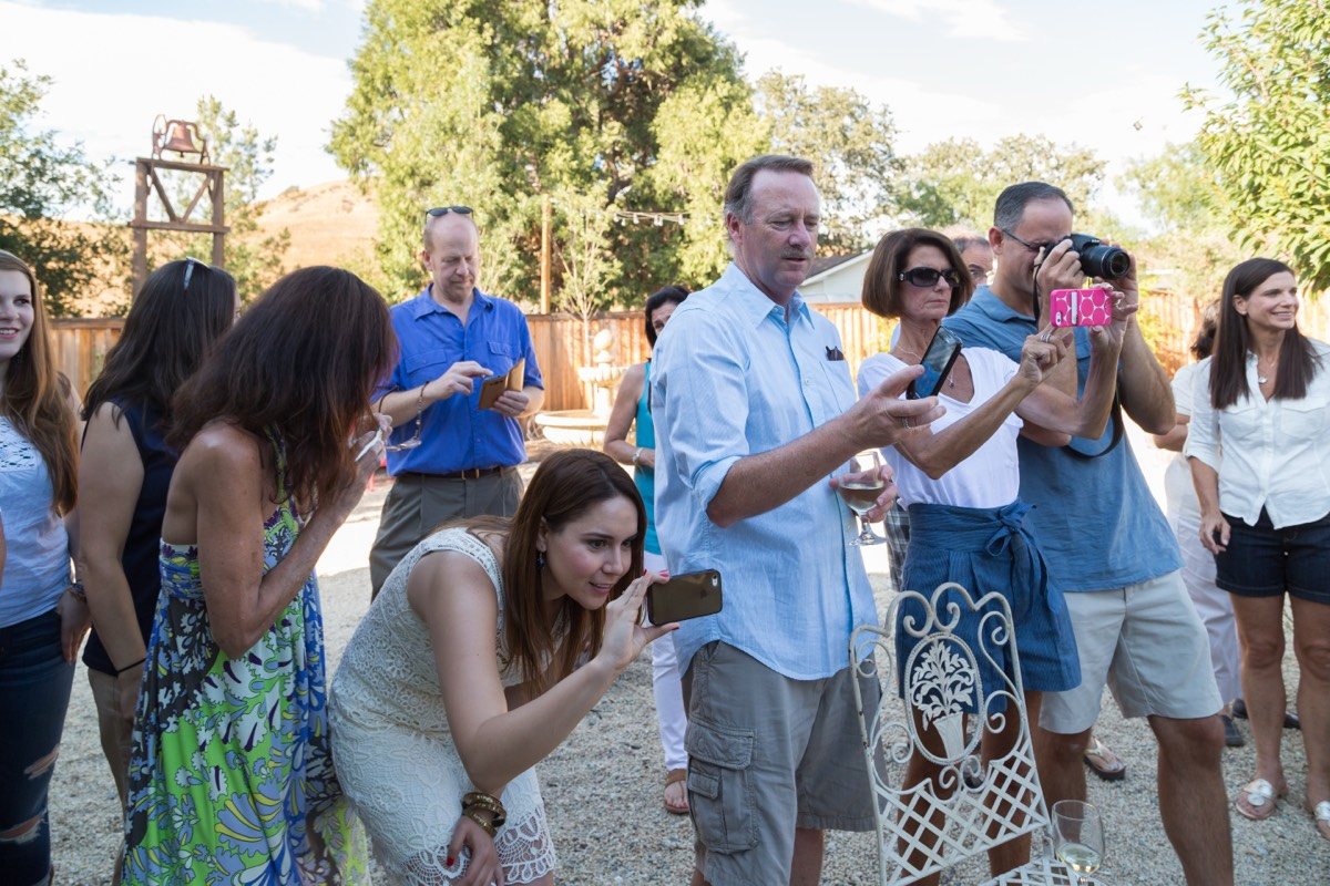 Guests crowding in to photograph the moment on their phones at an outdoor party