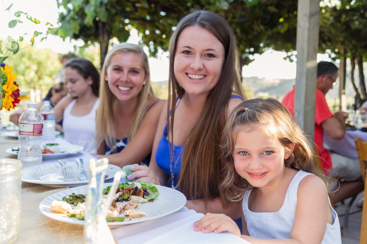 Young women and a girl smiling at a long outdoor party table