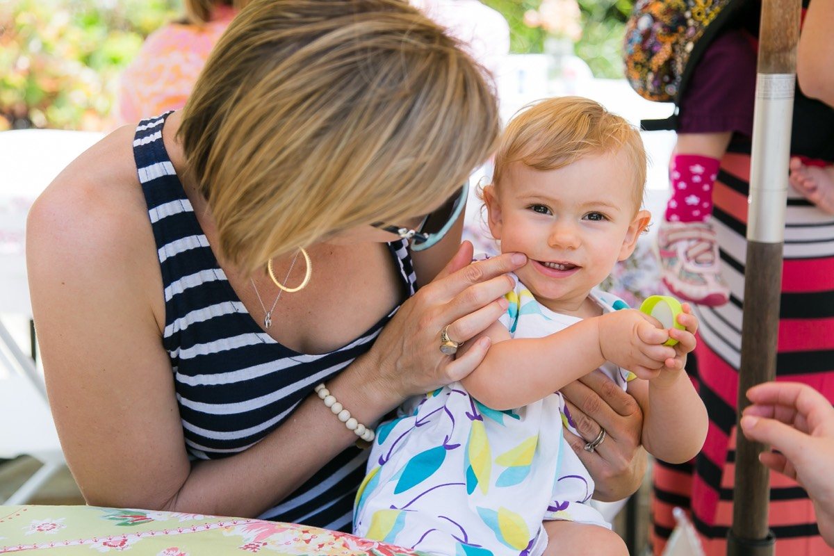 Woman kissing a smiling toddler on the cheek at a garden party