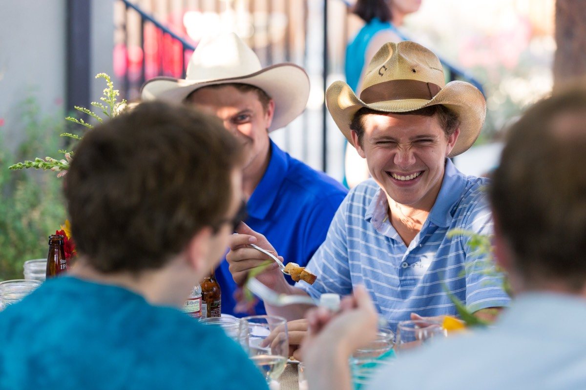 Guests in straw cowboy hats laughing at an outdoor party table