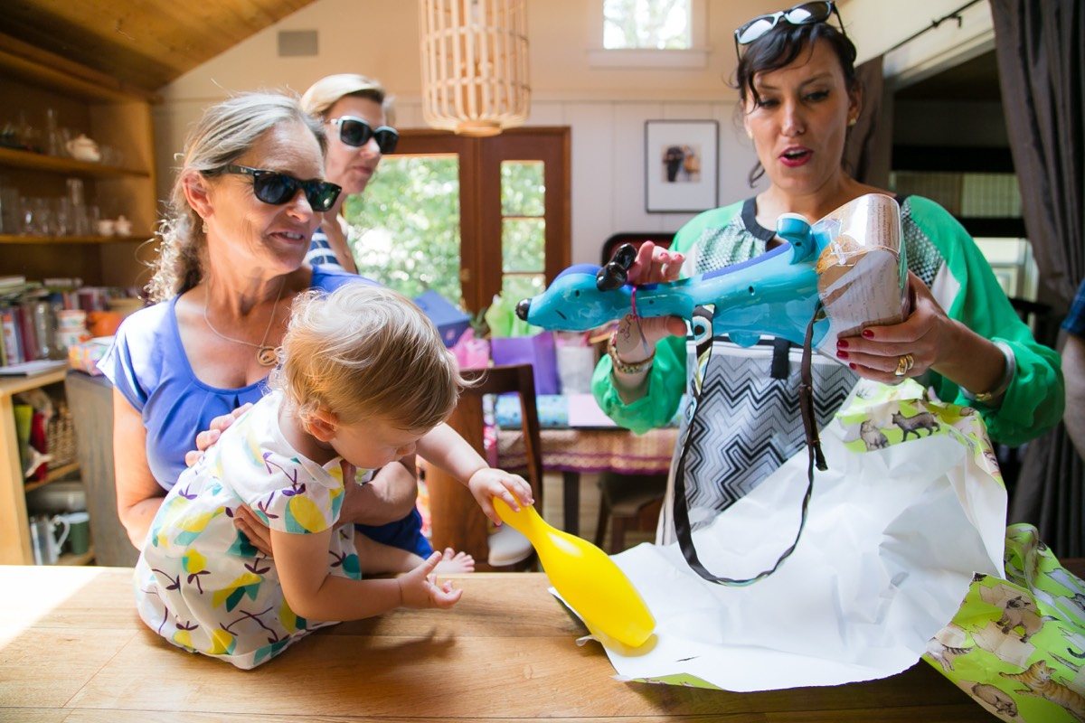 Toddler reaching for a gift on a table as women look on