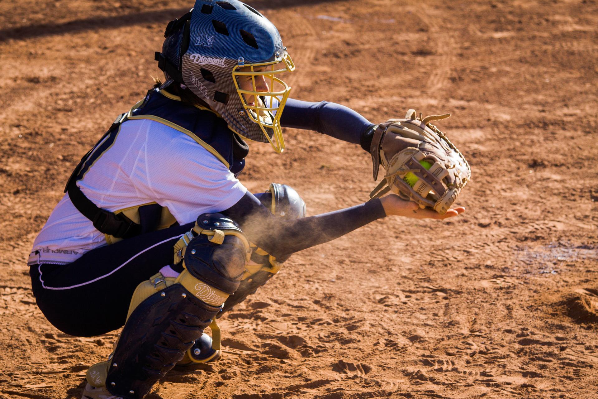 Softball catcher diving for a ball as dust flies at home plate