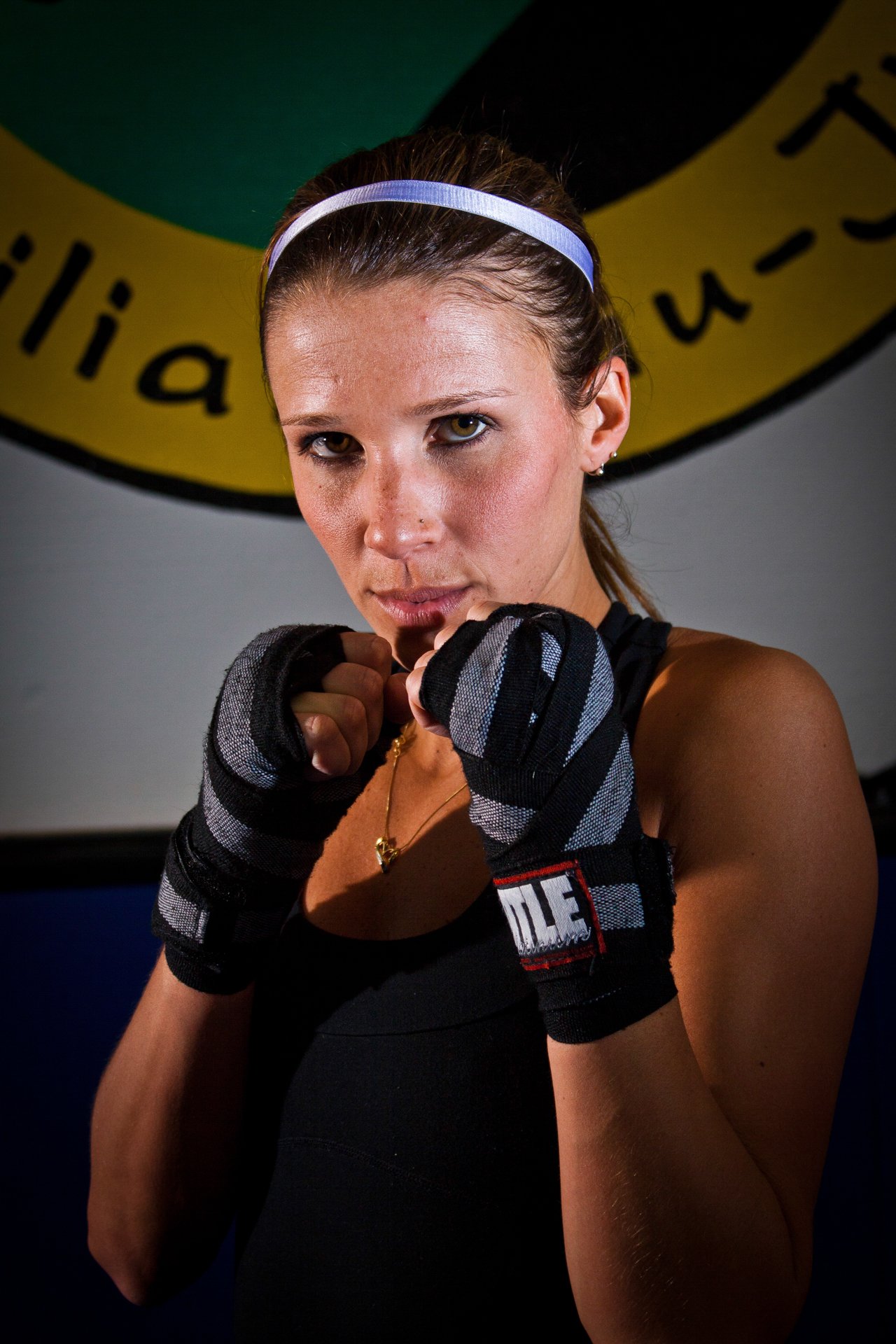 Boxer in wraps holding a guard, staring down the lens in a gym, dramatic flash